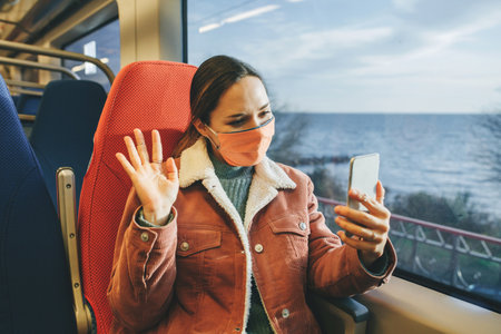 A girl in a protective face mask on the train communicates online. Traveling by train or commuter travel.の写真素材