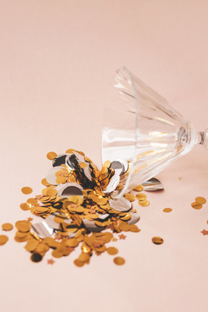 Wine glass with gold sparkles or confetti on a pink background. Celebration concept.の写真素材
