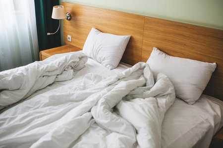 View of a rumpled bed with white pillows and a duvet.の写真素材