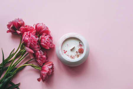Ecological and vegan handmade candle with dry flowers in a glass made of concrete on a pink background with pink tulips. Soy or coconut candle with a wooden wick.の写真素材