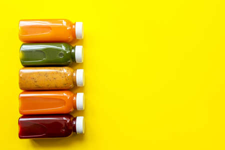 Fresh juices or cocktails of fruits and vegetables in bottles on a yellow background. The concept of...