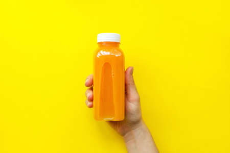 Female hand holding plastic bottles with orange juice or smoothie on yellow background. The concept of diets, detox. Bright background, flat lay, top viewの写真素材