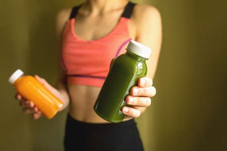 A female athlete holds bottles of freshly squeezed vegetable or fruit juice in her hands. The concept of a healthy lifestyle, a healthy bodyの写真素材