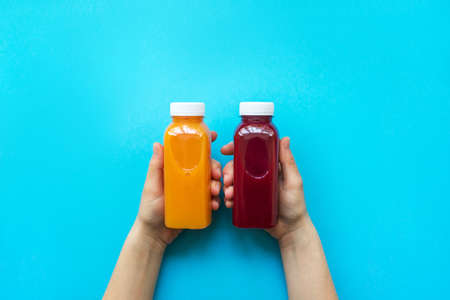 Female hands holding plastic bottles with orange juice or red smoothie on blue background. The concept of diets, detoxの写真素材