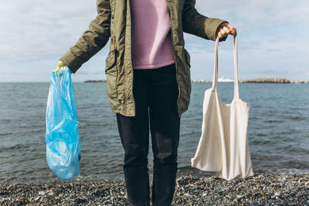 A female volunteer holds a garbage bag and a reusable canvas bag in her hands. The concept of waste...