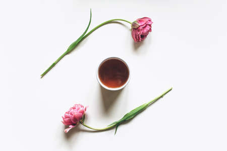 A cup of coffee or tea on a white background with pink tulips. Flat lay, top view.の写真素材
