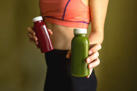 A female athlete holds bottles of freshly squeezed vegetable or fruit juice in her hands. The concept of a healthy lifestyle, a healthy bodyの写真素材