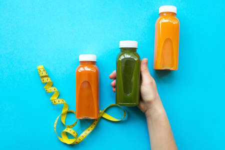 Female hand holding plastic bottles with juice or smoothie on blue background. The concept of diets, detoxの写真素材