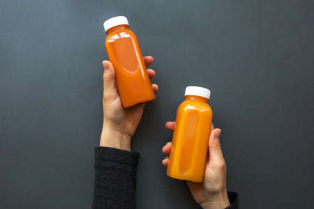 A woman is holding an orange detox juice or smoothie on a gray background. The concept of diets, detoxの写真素材