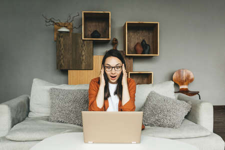 A very surprised young woman with glasses works from home.の写真素材