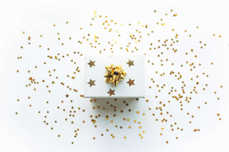 Gift white box with a gold tape and sequins on a white background. Celebrating Christmas or New Years or winning a prize or a promotion or other holiday concept. Flat lay, top viewの写真素材