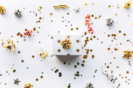 Gift white box with a gold tape with tinsel and confetti on a white background. The concept of a gift, a new year, a festive background. Flat lay, top viewの写真素材