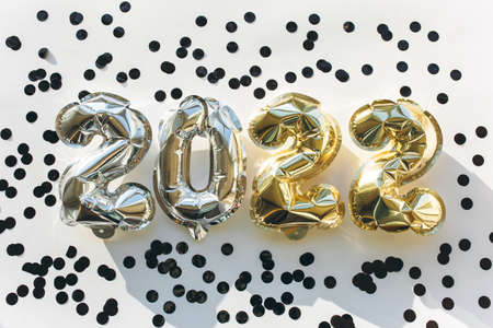 Balloons made of gold and silver foil in the form of numbers 2022 with confetti on a white background . Celebrating Christmas, New Year and festive concept. Flat lay, top view.の写真素材