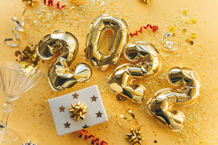 Balloons made of gold foil in the form of numbers 2022 with confetti on a gold background ....