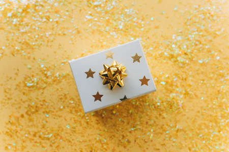 Gift white box with a gold tape with tinsel and confetti on a white background. The concept of a gift, a new year, a festive background. Flat lay, top viewの写真素材