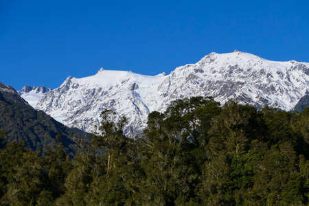 Side view of slightly snow covered mountain peaks with blue cloudless sky in early winter and trees in frontの写真素材