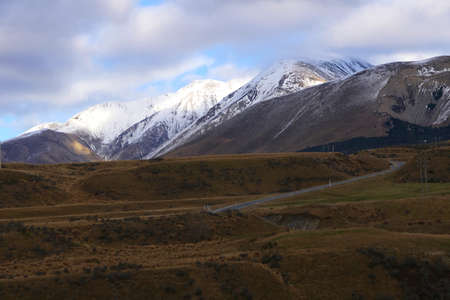 Road through the slightly snow covered Southern Alps in Canterbury New Zealand in the morning with clouds in the skyの写真素材