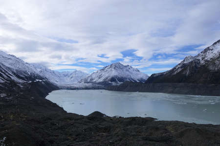 Hiking paradise - beautiful scenic frozen lake in the wintry New Zealand surrounded by snow covered mountains and clouds on a blue skyの写真素材