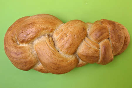Closeup fresh homemade braid or plaited bread from above on a green carving board ready for a sunday...