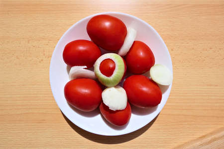 Salad ingredients - top view of a white plate with tomatoes and chopped onions outside on a wooden tableの写真素材