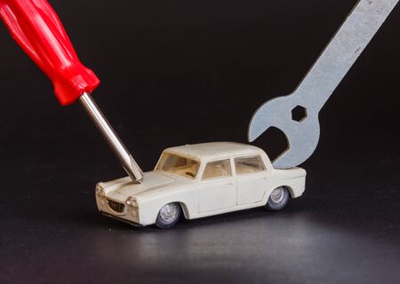 a screwdriver and a wrench are focused on a model of a car to represent a repairの写真素材