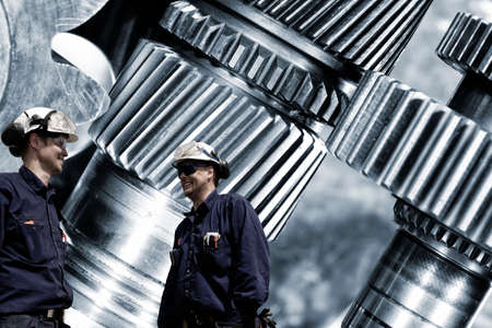 titanium and steel cogwheels with two mechanics in hard-hatsの写真素材