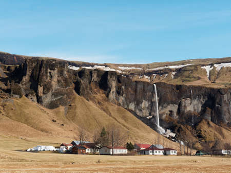 Basalt cliff, Foss a Sidu waterfall and farm, with blue sky in winter seen from road 1, southern Icelandの写真素材