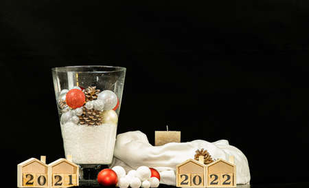 Glass vase filled with Christmas balls, cones and snow on black background with dates, cloth and...