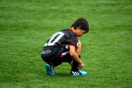 SAO PAULO, BRAZIL - SEPTEMBER 26, 2015: Young Boy tying boot on football field during rain.のeditorial素材