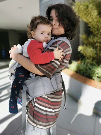 Older brother carrying little sister in the sling.