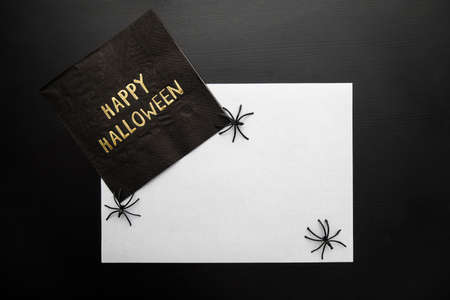 Top view a Napkin written Happy Halloween on dark background with some spiders. Copy space.