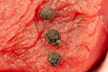 raw beef meat and black peppercorns close up