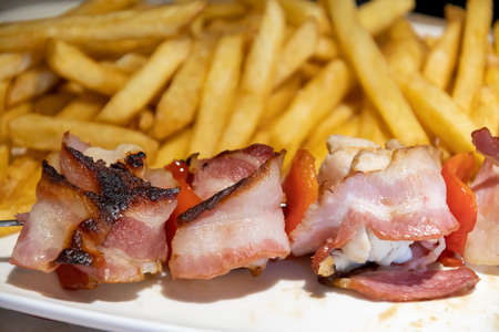 larded chicken skewer and fries on a plateの写真素材