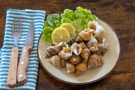 top view of cooked whelks on a plate with salad and lemonの写真素材