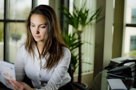 woman sitting behind a desk wearing white shirt in an officeの写真素材