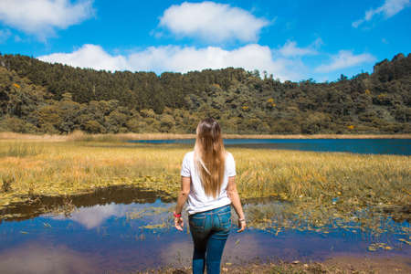 A beautiful woman on the lake watching the mountains and skyの写真素材