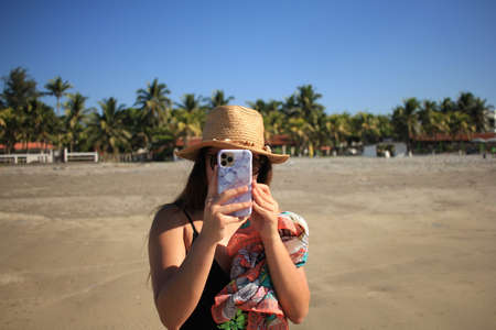 A Woman in hat using smart phone on the beach in summer. Vacation. Mobile Communication, Connection Conceptの写真素材