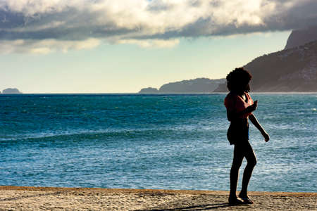 Girl walking in front of the sea and looking at the cell phone during the afternoon