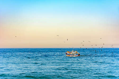 Old wooden fishing trawler sailing the sea with seagulls aroundの写真素材