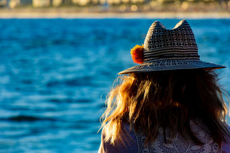 Woman with flower hat looking at the sea during the afternoonの写真素材