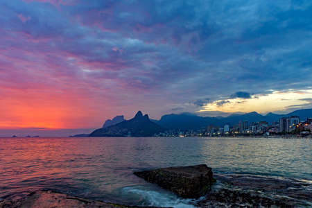 Summer sunset with cloudy sky with Two Brothers hill and Vidigal slum view from Ipanema beach at Rio...