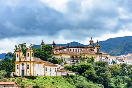 Ancient historical churches among the houses and streets of Ouro Preto city in Minas Gerais with hills and clouds in the backgroundの写真素材