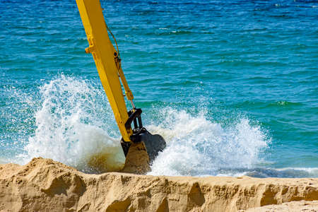 Backhoe removing sand from the beach and playing in the sea water that ends up splashingの写真素材