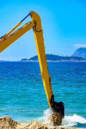 Backhoe removing sand from the beach and throwing in the sea to unclog the passageの写真素材