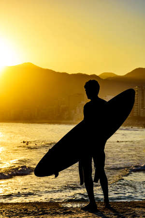 Surfer silhouette with his longboard looking at the Iapnema beach waves in Rio de Janeiro during sunsetの写真素材