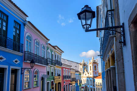 Old facades of colorful colonial-style houses and the tower of an old baroque church in Pelourinho,...