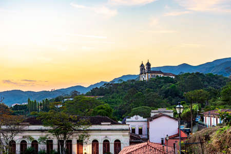 Old church on top of the hill with the city of Ouro Preto, hills and vegetation around during the sunsetの写真素材