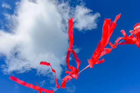 Decorative vivid red ribbons prepared for a religious festival in the city of Lavras Novas in Minas Gerais swaying in the wind with blue skyの写真素材