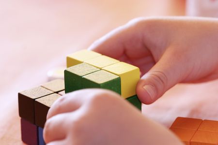 child's hands buliding a cube with gaming pieces
