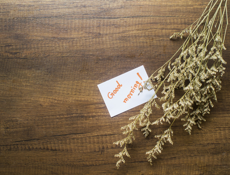 Flower and piece of paper with text "good morning" on the wooden table close-upの写真素材